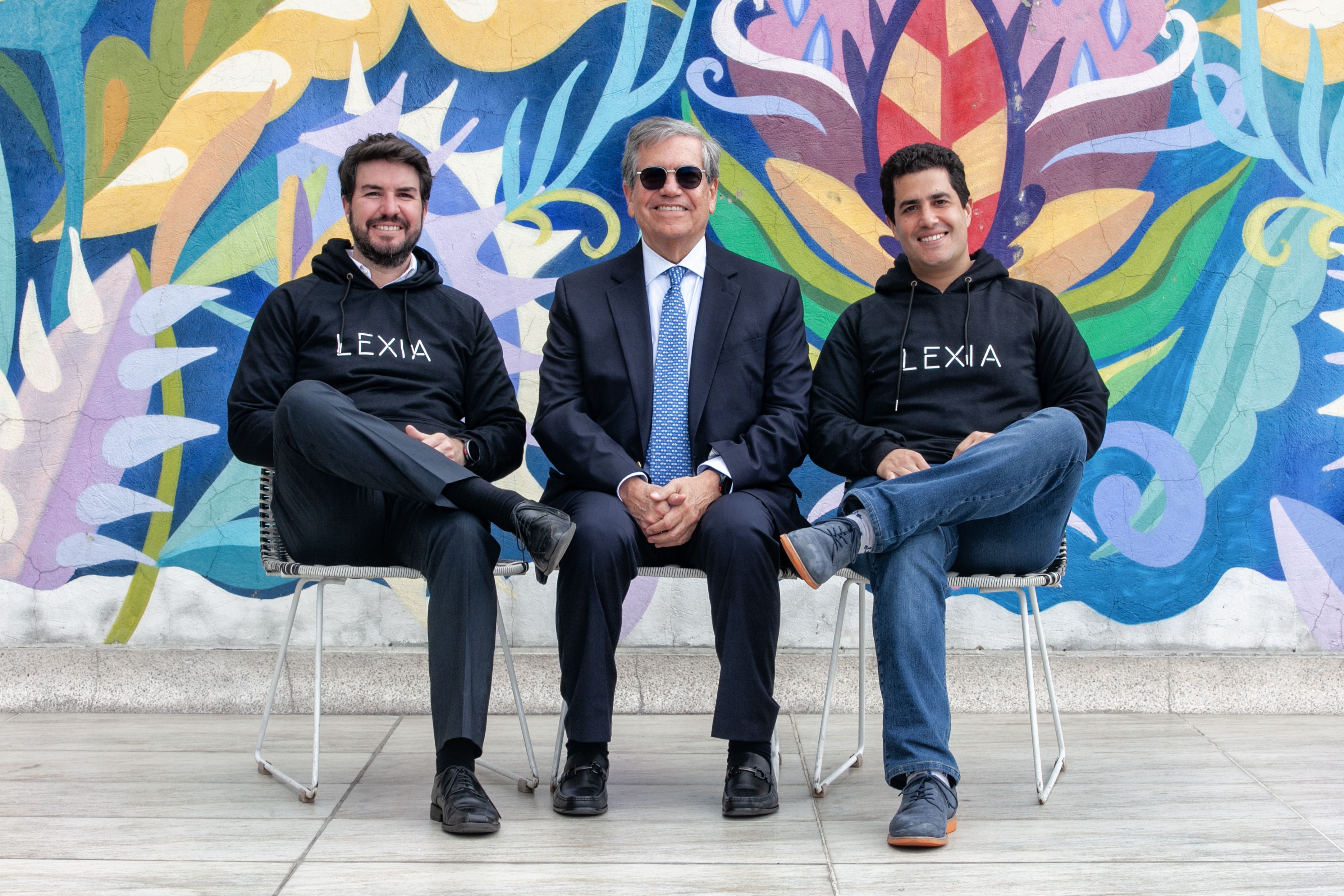 Los tres socios de Lexia Abogados sentados frente a un mural, con buzos de la firma